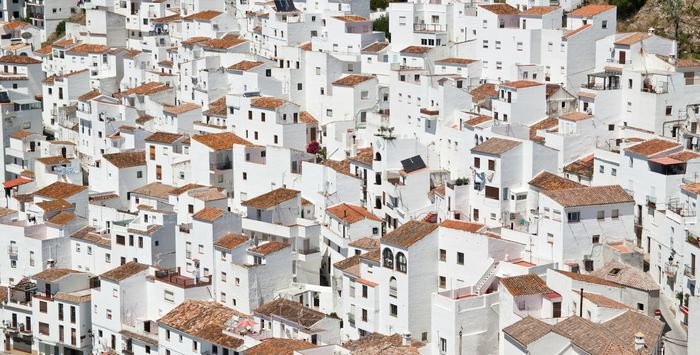 A dense hillside of Spanish houses filling the frame — white walls, terracotta roofs, roof terraces, washing on lines.
